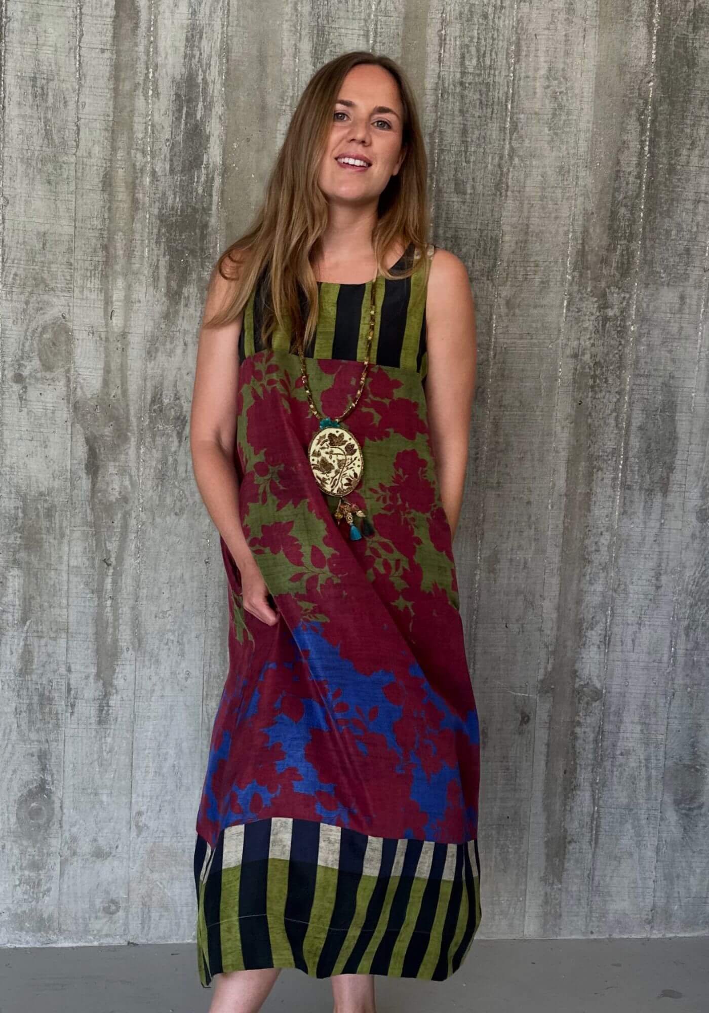 Woman wearing a colorful patterned dress against a textured wall.