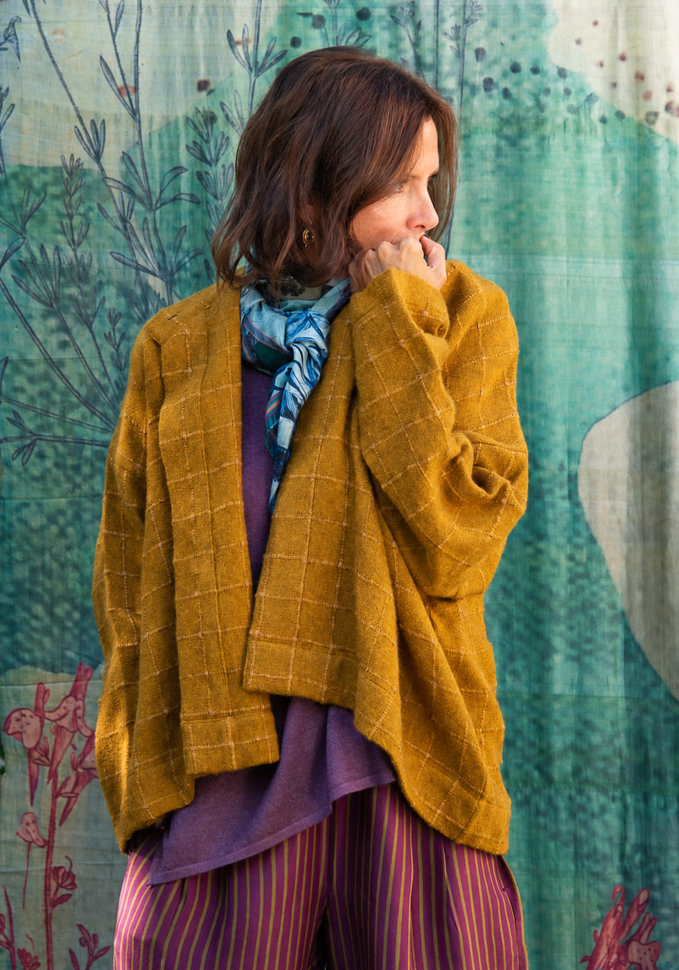 Mustard cardigan with a blue scarf over a purple outfit against the blue backdrop.