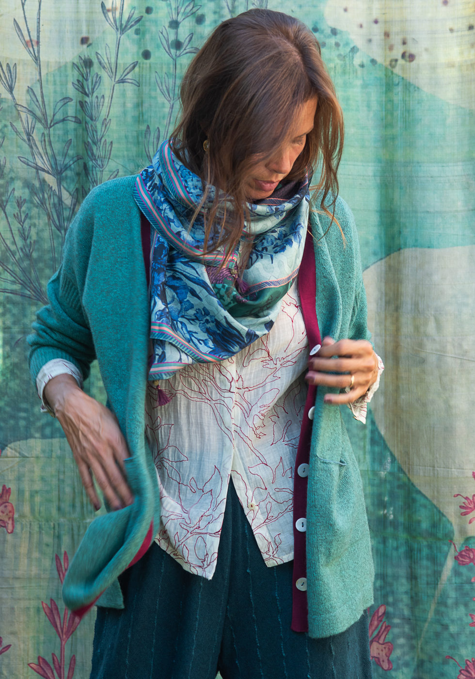 Turquoise cardigan over a white shirt with a scarf against the blue backdrop.