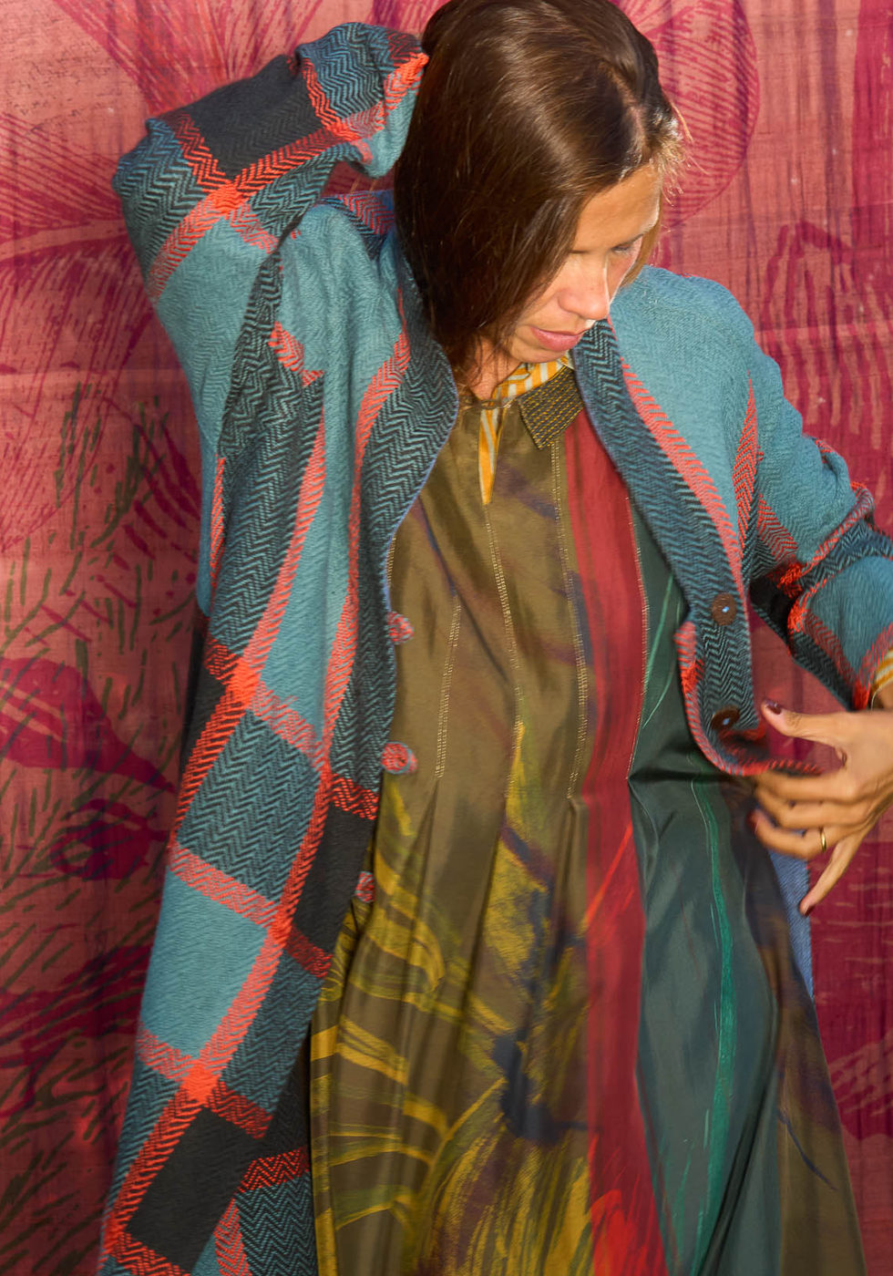 Blue and coral coat over a printed dress against the red backdrop.