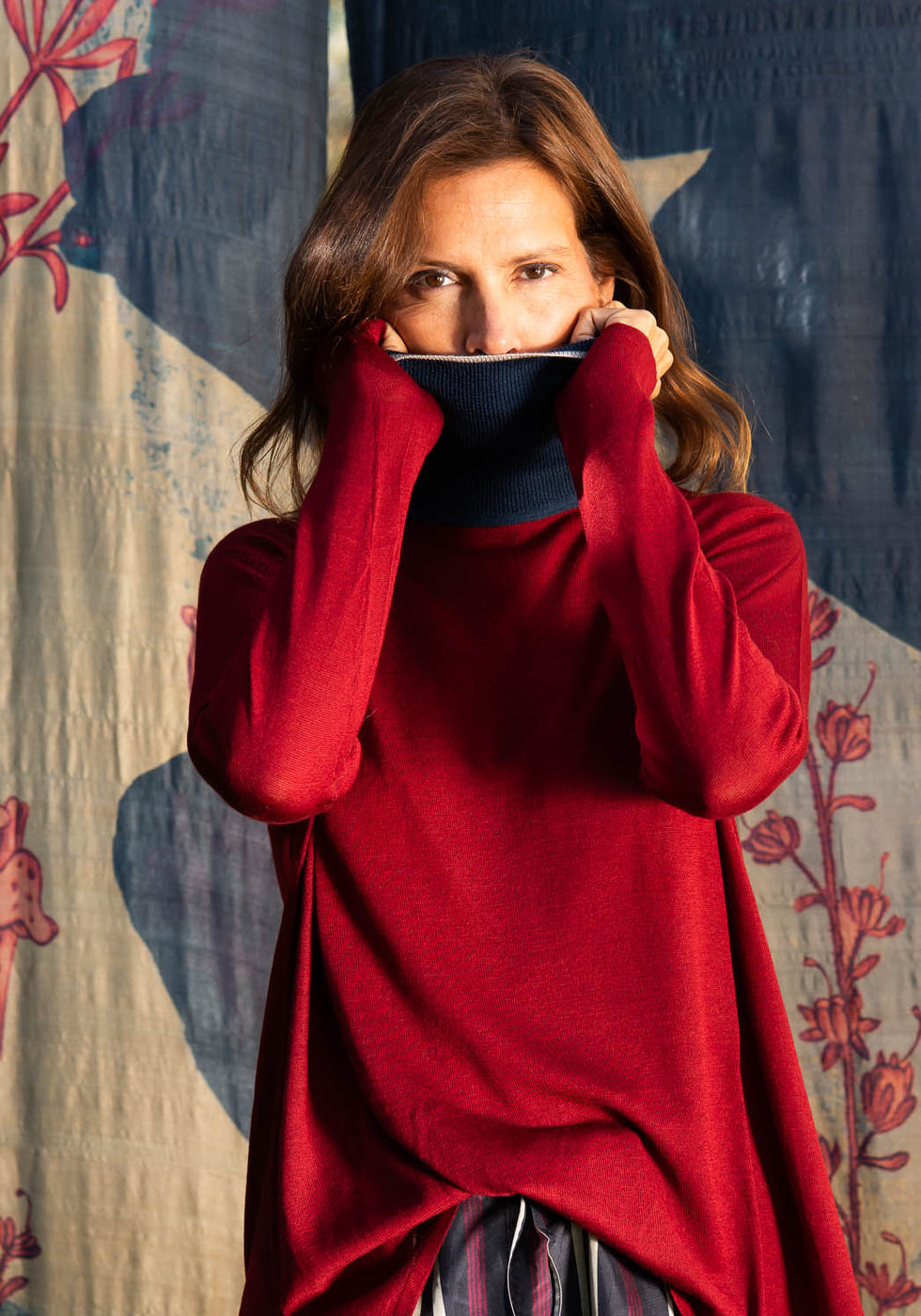 Red roll-neck jumper over a striped skirt against the dark blue botanical backdrop.